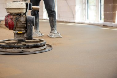 Bir inşaat işçisi, koruyucu ayakkabılar giyerek betonu güçlü bir malayla perdeledi. Yeraltı ısıtma boruları yüzeyin altına yerleştirildi.