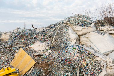 Büyük plastik atık yığınları, eski şişeler ve öğütülmüş malzemeler, yırtık endüstriyel torbalar ve açık hava ortamında makineler..