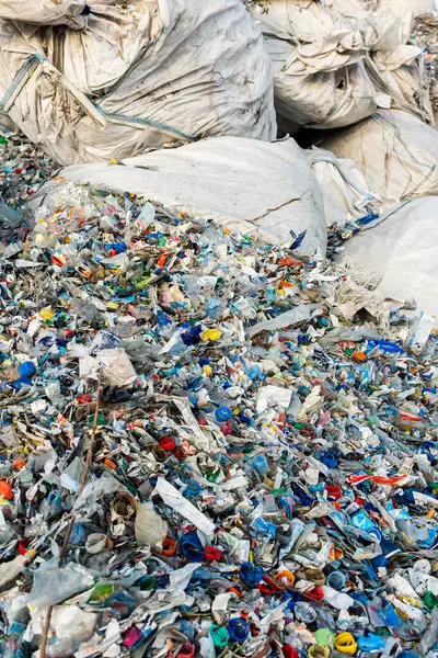 Renkli şişe kapakları ve parçalanmış parçalar da dahil olmak üzere kaotik bir plastik atık karışımı. Toplama veya depolama için kullanılan büyük beyaz çuvallarla çevrili..