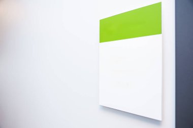 Sağında koyu dikey kenarı olan düz beyaz bir duvara dayalı, beyaz tabanlı, yeşil tabanlı modern bir tabela..