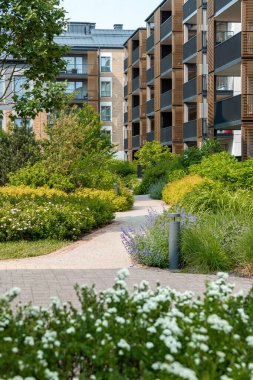 Ahşap aksanlı ve geniş pencereli çok katlı binalar canlı bitkiler, çiçekler, ağaçlar ve çalılarla dolu bir bahçenin etrafını sarar..