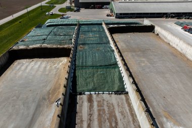 Yeşil muşambaları, beton duvarları, sanayi binaları, araçları ve ekipmanları olan sığınakları gösteren büyük bir tarım tesisi.