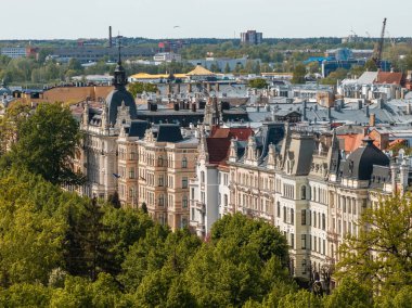 Dikenli çatıları olan tarihi binalar ön planda ağaçlar ve Letonya 'nın Riga kentindeki modern binalar.