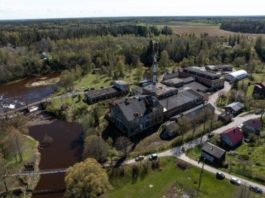 Uzun bir bacası, büyük binaları, tarlaları, ormanı ve dağınık evlerle çevrili barajı ve yaya köprüsü olan bir nehir..