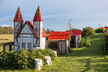 Kırmızı uçlu çatıları, yakındaki tavşan kafesleri, yeşil çimenler, bitkiler, ağaç kütükleri ve açık arazileri olan kaprisli bir şato..