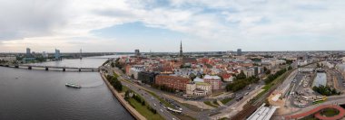 Aerial view of Riga, Latvia, highlighting the Daugava River, a bridge, St. Peter's Church spire, urban roads, railways, and a bus terminal.