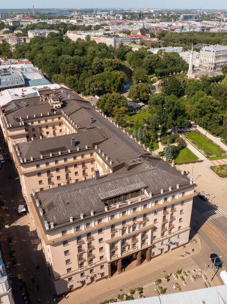 Aerial view of a U shaped building in Riga, Latvia, surrounded by parks and tree lined streets, with the Monument of Freedom visible near the center right.