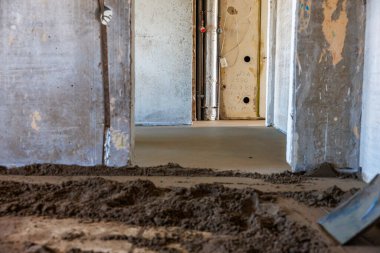 İçerisi inşaat halinde, beton duvarlar, açıkta kalan borular, kablolar, gevşek toprak ve ortada pürüzsüz dökülmüş bir yüzey..