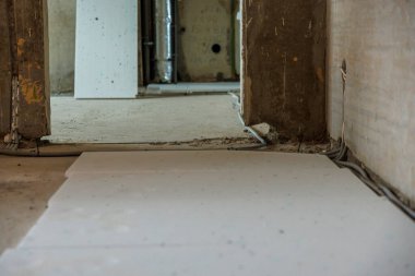 Kısmen kaplanmış zemin beyaz paneller, açıkta kalan beton duvarlar görünür kablolar ve endüstriyel inşaat ortamında metalik bir boru..