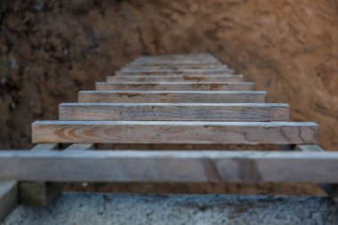 Yıpranmış ahşap bir merdiven çıplak toprakla çevrili bir toprak çukuruna iniyor, bir kazı veya inşaat alanı ayarını vurguluyor..