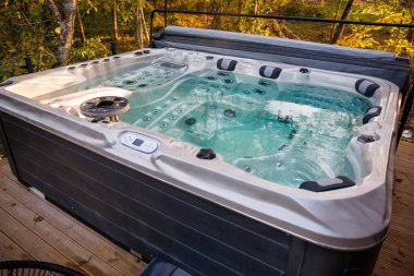 Jetleri ve ergonomik koltukları olan şık bir jakuzi ahşap bir güvertede duruyor. Sonbahar renkli ağaçlarla çevrili berrak suları doğal ışığı yansıtır..