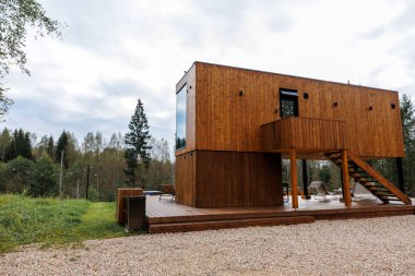Dikdörtgen ahşap kulübe, balkon, dış merdiven ve açık hava koltukları ile yükseltilmiş. Çimenler, ağaçlar ve çakıl yollarıyla çevrili..