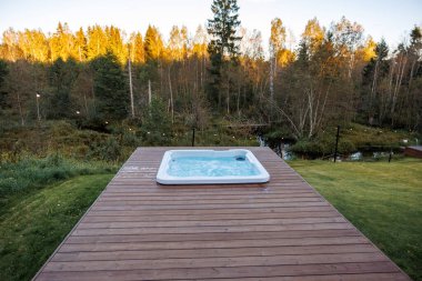 Bir jakuzili ahşap bir güverte ve sonbahar ağaçlarının olduğu bir açık alanda ip ışıkları kurulur. Güverte gün batımında küçük bir su özelliğini gözden kaçırıyor..