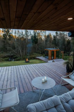 Yastıklı koltukları olan, şömine başında mumlar yakan ve ağaçlarla çevrili ahşap bir yapı olan modern bir ahşap güverte..