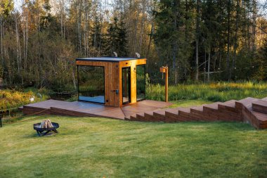 Çimlerle ve uzun ağaçlarla çevrili, büyük cam pencereli küçük bir ahşap kulübe. Bir ateş çukuru ve sicim ışıkları ayarları güçlendirir.