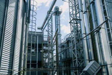 Yükselen metal siloları, çelik iskeletleri, merdivenleri ve parlak gün ışığı altında açık gökyüzü olan taşıyıcı sistemleri olan bir endüstri tesisi..