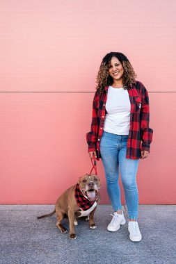 Caddede sevimli köpeğinin yanında kıvırcık saçlı neşeli Afrikalı kadın..