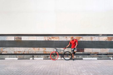 Güvenlik kaskı takmış, bisikletinin yanında gülümseyen ve caddede kameraya bakan Afrikalı Amerikalı teslimatçı..