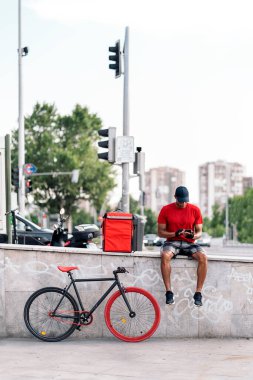 Sokakta oturan Afrikalı kurye telefonunu kullanarak bir paket teslim etmek için yoluna ara veriyor..