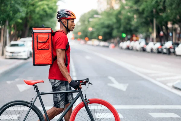 提着包裹 戴着安全帽 骑着自行车穿过城市的成年送货人 — 图库照片