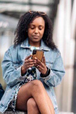 Renkli elbiseli güzel Afrikalı kız cep telefonuyla yazı yazıyor ve şehirde eğleniyor..