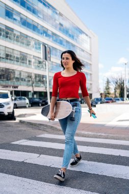 Bir elinde cep telefonu diğer elinde uzun panosuyla Zebra ile karşıya geçen sıradan elbiseli genç bir kadın..