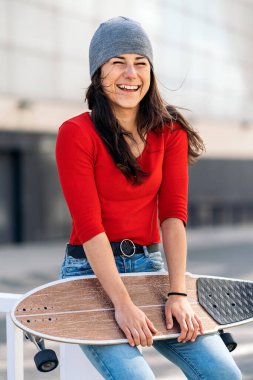 Uzun panosunu tutan, gülen ve kameraya bakan gündelik kıyafetleriyle mutlu genç bir kadın..