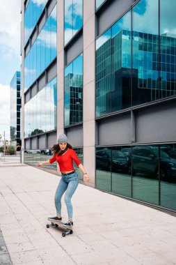 Havalı bir kaykaycı kadın şehirde uzun kaykayıyla pratik yapıyor ve eğleniyor..