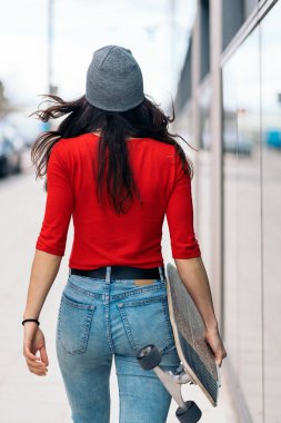 Tanımlanamayan kaykaycı kız sokakta yürüyor ve uzun kaykayını tutuyor..