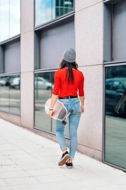 Tanımlanamayan kaykaycı kız sokakta yürüyor ve uzun kaykayını tutuyor..