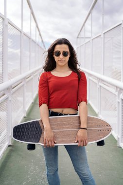 Şehirde sörf tahtasını tutan ve kameraya bakan sıradan bir genç kadın..