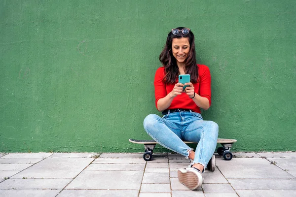 幸せな若いです女性座っている彼女の長いボードで緑の背景と彼女の携帯電話を使用して — ストック写真