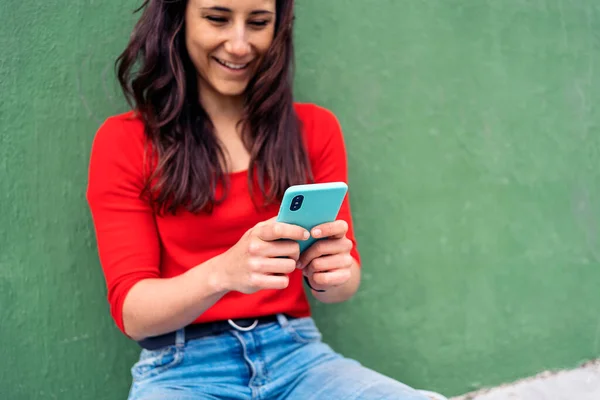 幸せな若いです女性座っている彼女の長いボードで緑の背景と彼女の携帯電話を使用して — ストック写真