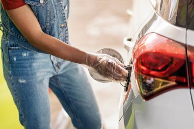 Benzin istasyonunda arabasına benzin dolduran plastik eldiven takan yüzü olmayan siyahi kadın..