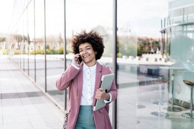 Afrika kökenli Amerikalı iş kadını şık kıyafetler giyiyor cep telefonunu açık havada kullanıyor ve konuşuyor..