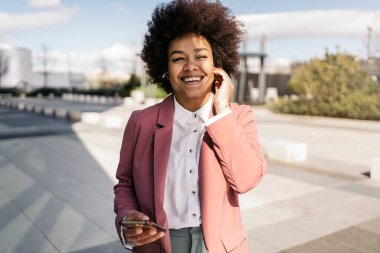 Afrika kökenli Amerikalı iş kadını şık kıyafetler giyiyor cep telefonunu açık havada kullanıyor..