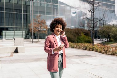 Afrika kökenli Amerikalı iş kadını şık kıyafetler giyiyor cep telefonunu açık havada kullanıyor ve konuşuyor..