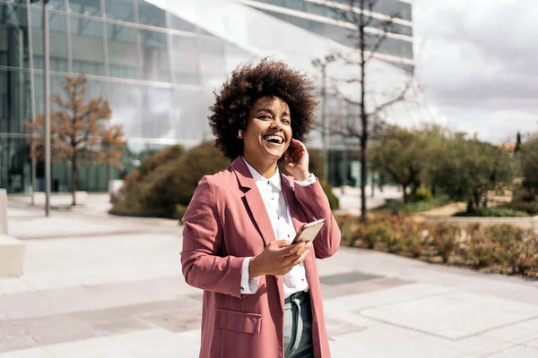 アフリカの髪の笑顔とビジネスエリアで屋外で彼女の携帯電話を使用して幸せな黒人ビジネス女性 — ストック写真