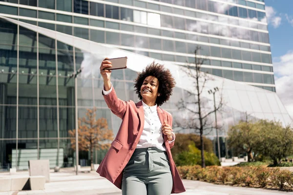 Happy black business woman with afro hair smiling and taking selfie with her mobile phone.