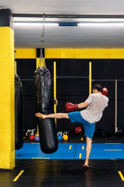 Kickboks dövüşçüsü spor salonunda ayaklarıyla kum torbasına tekme atıyor. Kickboks kavramı.