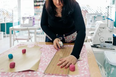 Parlak moda atölyesinde tanınmayan bir kadın çalışıyor. Kumaşları ölçüyor..