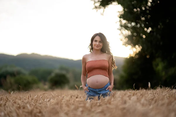 孕妇笑着站在麦田里 她在看相机 — 图库照片