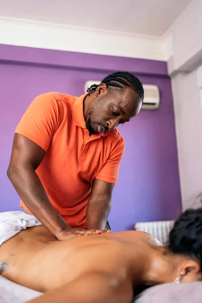 Relaxed woman lying down and receiving a back massage. The masseuse is a handsome african american man.