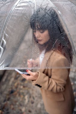 Yağmurlu bir günde sokakta şemsiyesi olan tanınmamış genç bir kadın cep telefonunu kullanıyor..