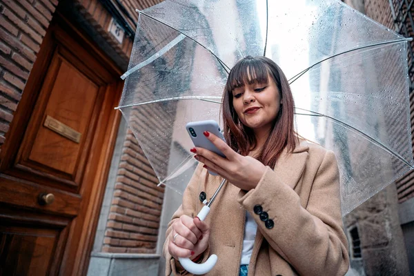 Mladá Žena Pomocí Průhledného Deštníku Deštivém Dni Pomocí Svého Mobilního — Stock fotografie