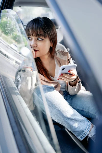 Szczęśliwa Kobieta Siedzi Samochodzie Używa Telefonu Komórkowego Sobie Makijaż Ubranie — Zdjęcie stockowe