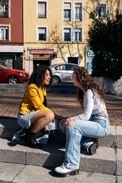 卷曲头发的姑娘们坐在街上互相望着 互相交谈着 他们在笑 玩得很开心 — 图库照片