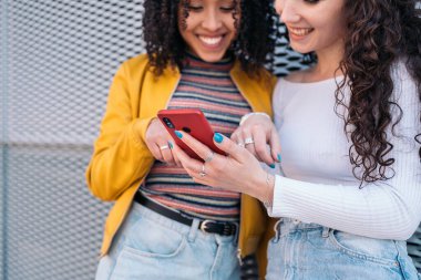 Kıvırcık saçlı, gülümseyen ve dışarıda cep telefonu kullanan güzel kızlar..