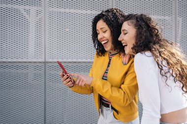 Kıvırcık saçlı güzel kızlar dışarıda gülüyor ve cep telefonu kullanıyor..
