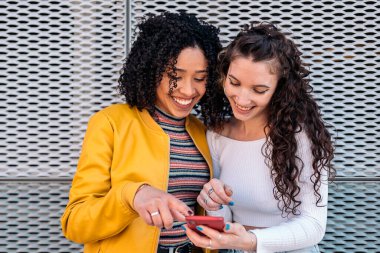 Kıvırcık saçlı, gülümseyen ve dışarıda cep telefonu kullanan güzel kızlar..